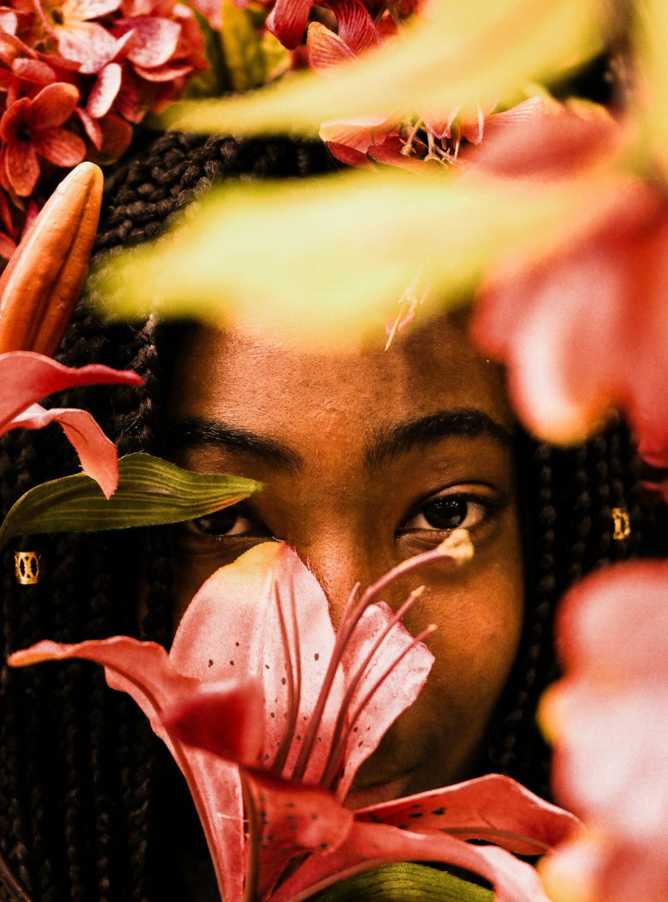 Close-up portrait of a young Black woman with braids surrounded by pink lilies and floral blooms